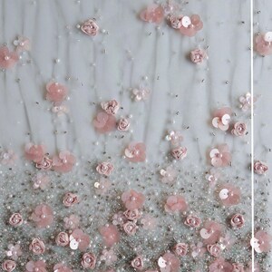 以下が含まれることがあります： 薄いグレーの生地にピンクの花の刺繍と白いビーズが施されたクローズアップ。刺繍は下部が濃く、上部に行くにつれて薄くなっている。テキスト「The embroidery continue to reduce in density moving upwards from the bottom edge.」と「Bottom Edge」が表示されている。