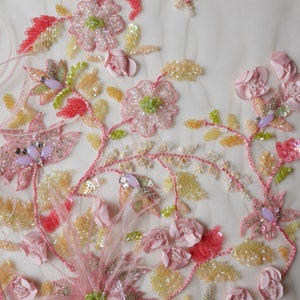May include: Close-up of delicate pink and yellow floral embroidery on a sheer fabric. The embroidery features beaded flowers, leaves, and stems, creating a beautiful and intricate design.
