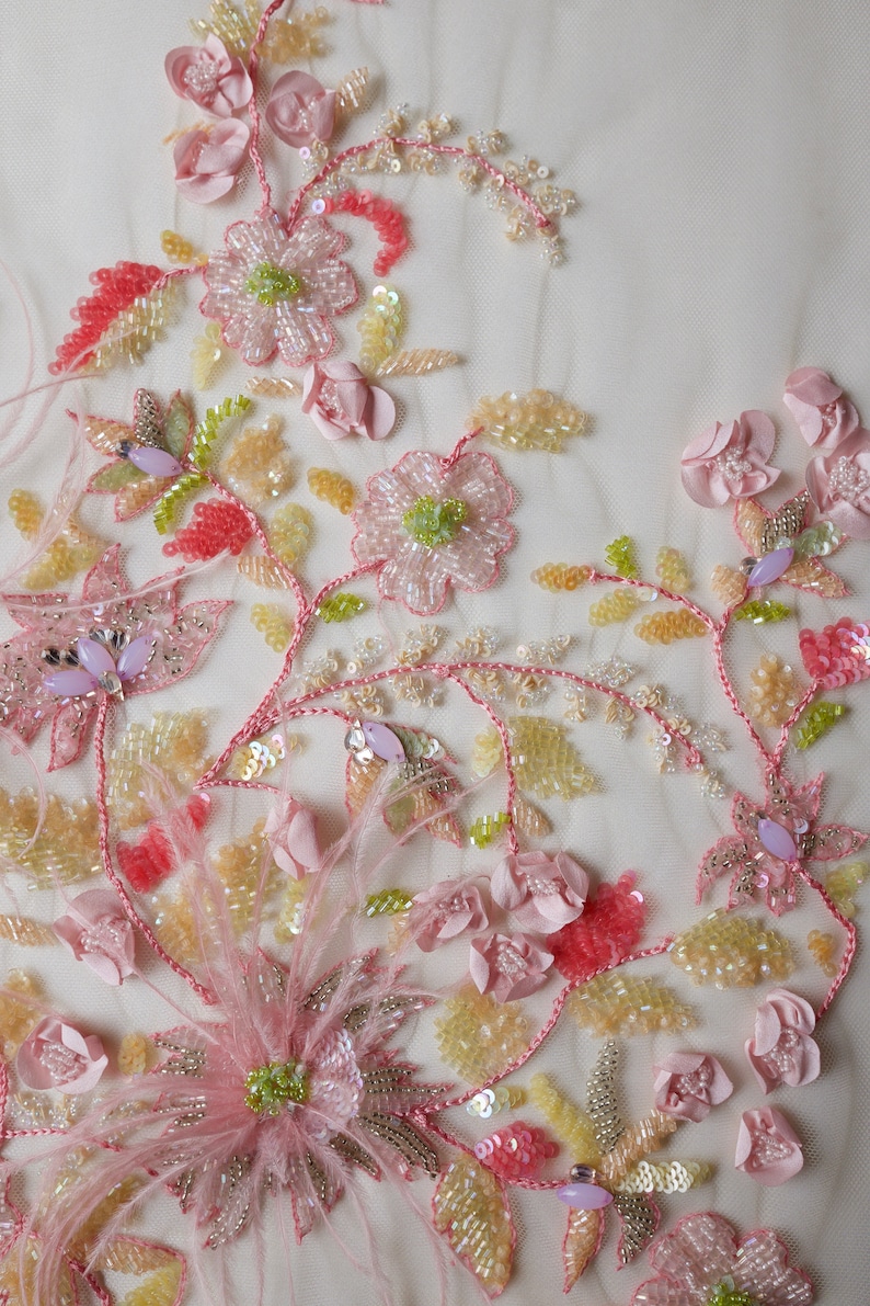 May include: Close-up of delicate pink and yellow floral embroidery on a sheer fabric. The embroidery features beaded flowers, leaves, and stems, creating a beautiful and intricate design.