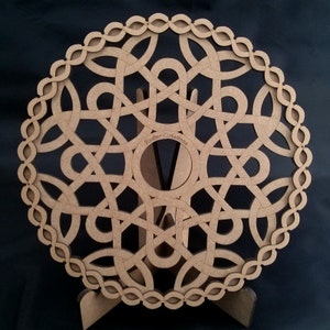 Peut inclure: Une décoration murale en bois brun avec un motif circulaire de nœuds complexes. Le motif est découpé dans le bois, créant un motif délicat et complexe. La décoration murale est sur un support en bois.