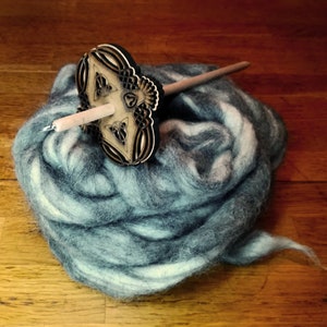 Peut inclure: Un rouet en bois avec un motif décoratif sur le dessus, reposant sur un tas de laine bleue et blanche.