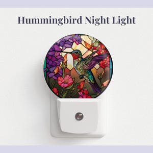 May include: A night light featuring a stained glass design of a hummingbird in flight surrounded by flowers. The hummingbird is blue, green, and purple, and the flowers are red, pink, and purple.