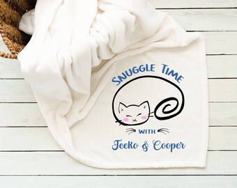 Pode incluir: Cobertor de lã branca com uma ilustração em preto e branco de um gato enroscado dormindo. O texto "Snuggle Time with Teeko & Cooper" está impresso em azul.
