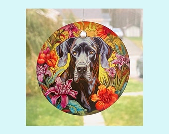 Pode incluir: Um ornamento de vidro redondo com um cão Dogue Alemão preto sobre um fundo floral. As flores são de cor vermelha, laranja, amarela, rosa e verde.