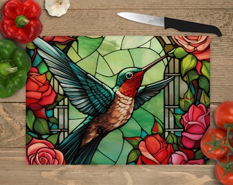 Pode incluir: Uma tábua de cortar de estilo vitral com um beija-flor em voo com detalhes vermelhos, verdes e azuis. O beija-flor é cercado por rosas cor-de-rosa e vermelhas.
