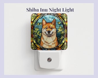 Pode incluir: Uma luz noturna branca com um design de vitral que apresenta um cão Shiba Inu. O cão é marrom e branco com o nariz e a língua pretos. O design de vitral é cercado por uma borda verde e marrom.