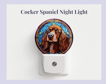 Pode incluir: Uma luz noturna de vidro colorido com um cão Cocker Spaniel marrom e branco em um fundo azul, verde e amarelo. A luz noturna está ligada a uma tomada elétrica.