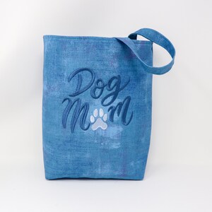 K&ouml;nnte beinhalten: Blaue Tragetasche mit dem gestickten Text "Dog Mom" in Wei&szlig; und Blau mit einem wei&szlig;en Pfotenabdruck.