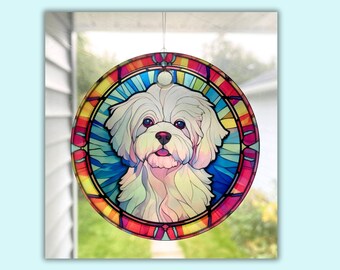 Pode incluir: Um ornamento de vidro colorido com um cão maltês branco sobre um fundo colorido. O ornamento é redondo e tem um esquema de cores vermelho, amarelo, azul e verde.
