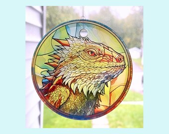 Pode incluir: Um apanhador de sol de vitral com uma ilustração colorida e detalhada da cabeça de um lagarto. O lagarto é amarelo, laranja e vermelho com uma aparência texturizada e escamosa.