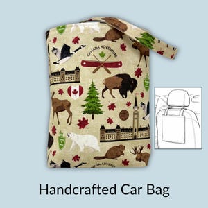 May include: Handcrafted car bag with a beige background and a repeating pattern of Canadian symbols, including a maple leaf, moose, bear, and the text "Canada Adventure". The bag has a handle and a diagram of how to attach it to a car seat.