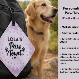 May include: A personalised paw towel with the text "LOLA'S Paw Towel" in a diamond shape, attached to a black backpack. The towel is light purple with paw prints and measures 30cm x 30cm. A golden retriever dog is in the background.