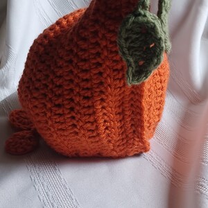 May include: Handmade orange crochet pumpkin with green leaves and stem. The pumpkin is made with a textured stitch and has a rounded shape. A charming fall decoration for the home.