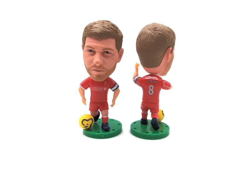 K&ouml;nnte beinhalten: Eine rote und wei&szlig;e Liverpool-Fu&szlig;ballspieler-Figur mit der Nummer 8 auf dem R&uuml;cken. Die Figur h&auml;lt einen gelben Fu&szlig;ball und steht auf einem gr&uuml;nen Sockel.