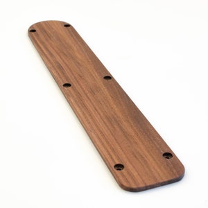 Könnte beinhalten: Ein langer, schmaler, hölzerner Türgriff mit abgerundeter Oberseite und dunkelbrauner Oberfläche. Der Griff hat mehrere kleine Löcher, die hineingebohrt wurden.