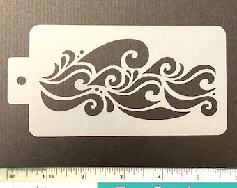 May include: A white plastic stencil featuring a stylized wave design. The stencil has a rectangular shape with rounded corners and a small tab with a hole on the left side. The image also includes a ruler and text that reads "Face Painting SUPPLIES".
