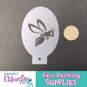 Könnte beinhalten: Eine silberne Bienen-Schablone zum Schminken, mit einer Münze zum Größenvergleich. Die Schablone hat eine abgerundete Form mit einem kleinen Loch am unteren Rand. Der Text "Face Painting SUPPLIES" befindet sich in der unteren rechten Ecke.