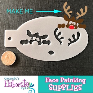 以下が含まれることがあります： トナカイのデザインが施された白いフェイスペイントステンシル。トナカイは茶色の角と赤い鼻をしています。ステンシルの隣にはコインがあります。「MAKE ME」と「Face Painting SUPPLIES」の文字が含まれています。