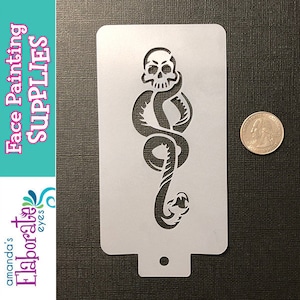 May include: A face painting stencil featuring a skull intertwined with a snake. The stencil is white and rectangular with rounded corners. The words "Face Painting SUPPLIES" are printed on the left side. A quarter is next to the stencil for size comparison.