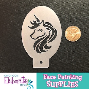 Puede incluir: Un esténcil de unicornio de color claro para pintar caras. El esténcil tiene forma ovalada con un diseño de unicornio recortado. La imagen también incluye una moneda para comparar el tamaño. El texto "Face Painting Supplies" está en la parte inferior.