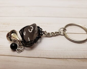May include: A black and silver keychain with a gray, clear, six-sided die, a black bead, and a silver charm. The die has white numbers on each side.