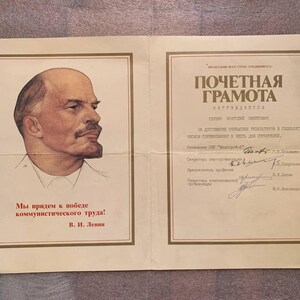 Puede incluir: Un certificado de honor soviético vintage impreso en papel color crema. El lado izquierdo presenta un retrato de Vladimir Lenin y el texto 'Мы придем к победе коммунистического труда! В. И. Ленин'. El lado derecho muestra 'ПОЧЕТНАЯ ГРАМОТА' con firmas manuscritas.