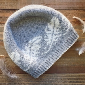Puede incluir: Un gorro de punto gris con un patrón de plumas blancas. El gorro está hecho de hilo suave y tiene un ajuste cómodo.