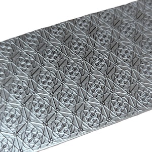 May include: A rectangular silver-coloured metal sheet featuring a repeating embossed geometric pattern. The design consists of interconnected circles and triangles, creating a grid of four-petaled floral shapes across the entire surface.