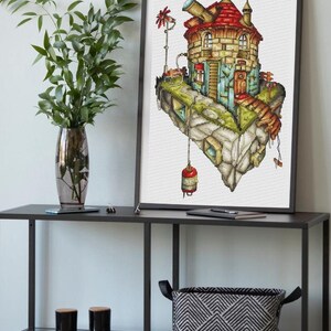 Peut inclure: Broderie encadrée représentant une île flottante fantaisiste avec une maison détaillée. La maison a un toit rouge, des fenêtres et un télescope. L'île est entourée d'un paysage rocheux et une lanterne rouge est suspendue en dessous. L'œuvre est exposée sur une étagère noire.