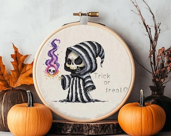 Può includere: Un ricamo a punto croce a tema Halloween in un telaio di legno. Il disegno presenta un cartone animato di Grim Reaper che tiene una testa di teschio fiammeggiante con il testo "Trick or Treat!". Due zucche arancioni e foglie autunnali in primo piano.