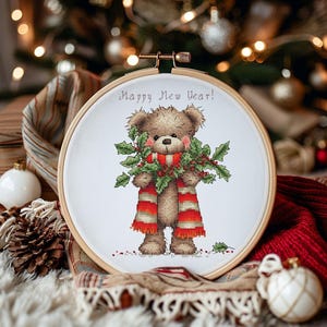 May include: Cross-stitch embroidery in a wooden hoop features a teddy bear wearing a red and orange striped scarf and holding holly. The text "Happy New Year!" is arched above the bear. Festive holiday decor.