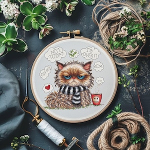 May include: A cross-stitch embroidery hoop showing a grumpy cat wearing a striped scarf. Text bubbles read "NOT TODAY", "I'M OVER IT", and "COFFEE". A red coffee cup with a smiley face is also included in the design.