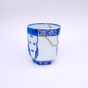 May include: A white ceramic cup with blue and gold painted designs. The cup has a crack that is repaired with gold tape.