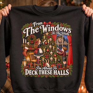 May include: A black crewneck sweatshirt featuring a graphic print of two children decorating a Christmas tree with skulls. The text reads, From The Windows To The Walls I'm About To Deck These Halls. The scene includes a fireplace, a witch, and greenery.