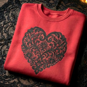 Puede incluir: Una sudadera roja con un gran diseño de corazón negro adornado. El corazón está lleno de intrincados patrones florales y de volutas, creando una estética elegante. La sudadera está hecha de un material suave.