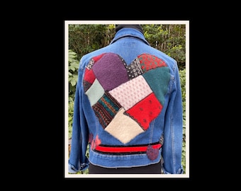 May include: A blue denim jacket with a large heart-shaped patch on the back. The patch is made of various colorful fabric scraps sewn together.