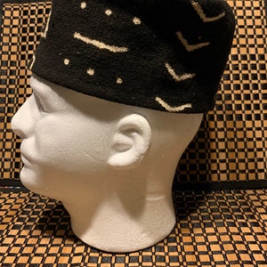 May include: A black and white patterned fabric hat with a geometric design. The hat is on a white mannequin head.