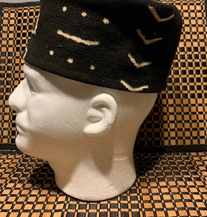 May include: A black and white patterned fabric hat with a geometric design. The hat is on a white mannequin head.