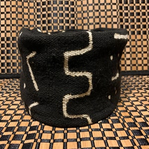 May include: Black and white woven basket with a geometric pattern. The basket is made of a soft, textured fabric.