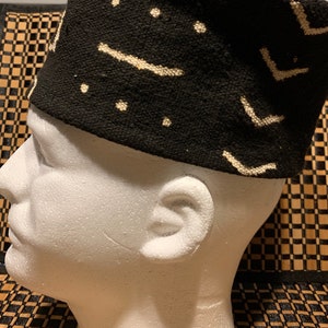 May include: A black and white patterned fabric hat with a geometric design. The hat is made of a soft, woven fabric and has a flat top.