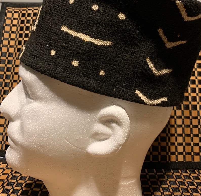 May include: A black and white patterned fabric hat with a geometric design. The hat is made of a soft, woven fabric and has a flat top.