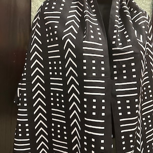 May include: Black and white patterned scarf with geometric designs. The scarf is made of a soft, lightweight fabric and features a variety of geometric shapes, including arrows, squares, and lines.
