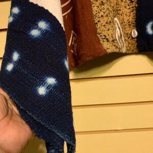 May include: A blue and white fabric with a pattern of small white circles. The fabric is folded in a triangular shape and is held in a hand.