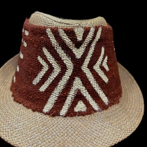 May include: A brown and beige straw hat with a brown band featuring a white geometric pattern.