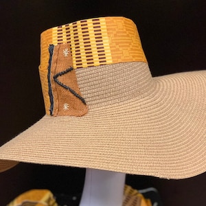 May include: A wide-brimmed straw hat with a brown and yellow patterned band. The hat has a brown fabric patch with white stitching and a black star design.
