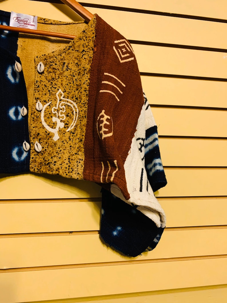 May include: A brown, white, and blue patterned cardigan with a button closure and a white design on the front. The cardigan is made of a woven fabric and has a relaxed fit.