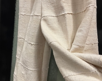 May include: A pair of off-white, wide-leg pants made from a woven fabric with a textured surface. The pants have a relaxed fit and are designed with a series of horizontal seams.