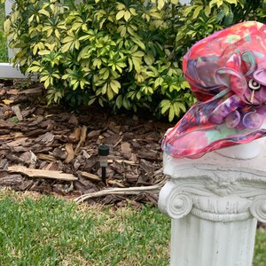 May include: A pink and red floral hat with a large flower accent sits on top of a white column.