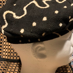 May include: Black and white patterned fabric hat with a white wavy design. The hat is on a white mannequin head.