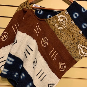 May include: A brown, tan, white, and blue patterned poncho with a button closure. The poncho has a geometric design with symbols and lines.